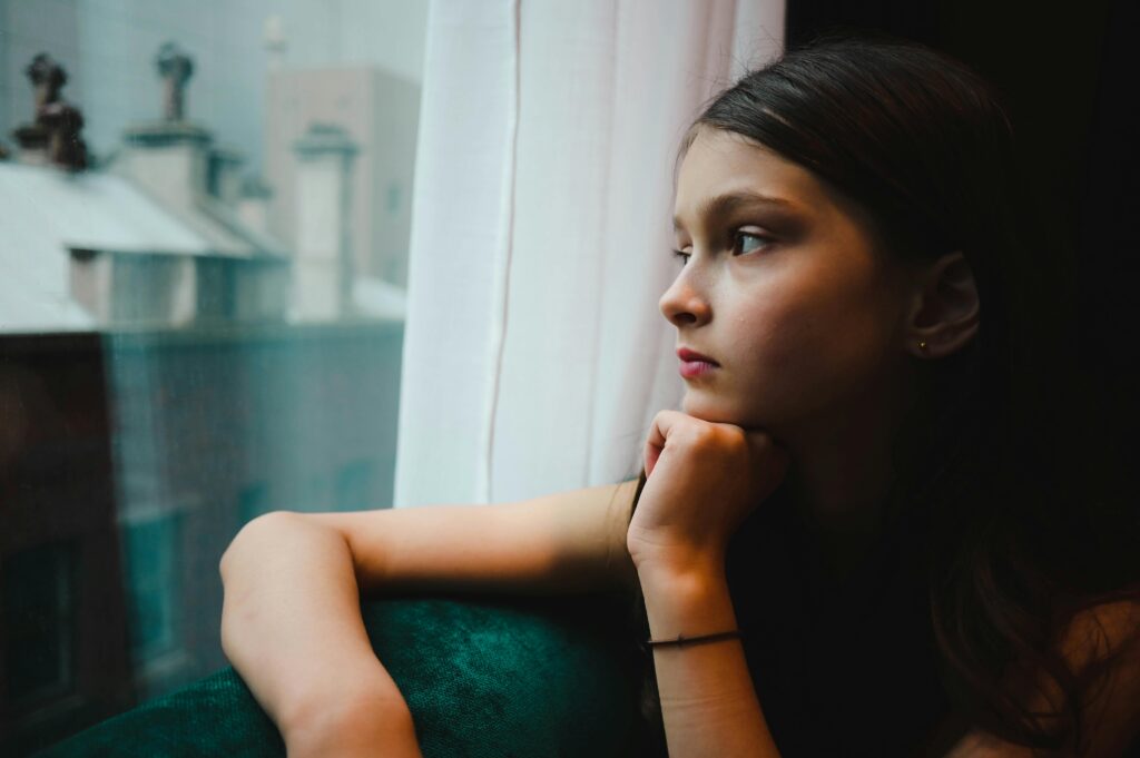 Adolescente regardant par la fenêtre, illustrant la fatigue sociale du TSA